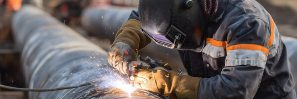 Soudage de pipelines sur un chantier industriel en plein air par un ouvrier en combinaison de protection. Soudage de pipelines sur un chantier industriel en plein air par un ouvrier en combinaison de protection.